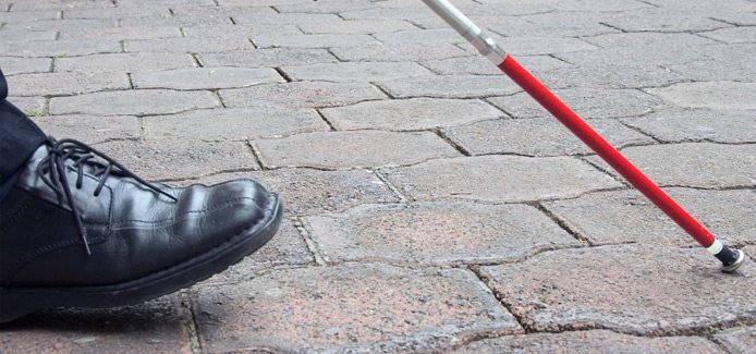 Close-up view of a persons shoe and White Cane while walking on a sidewalk