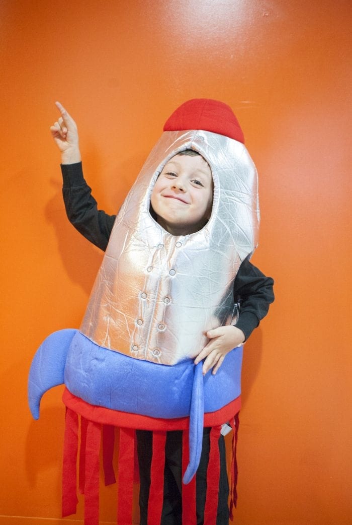 Image showing a young boy wearing a rocketship Halloween costume and pointing upward.