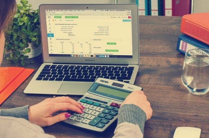 Image of a lady sitting at her desk with a 508 compliant banking document displayed on her computer screen and a large print calculator. Person's hands holding a calculator in front of a laptop