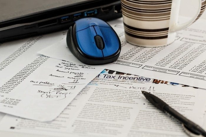 Image showing several tax and financial documents which should be made accessible for those with vision impairments. Computer mouse, mug, and pen on top of financial papers