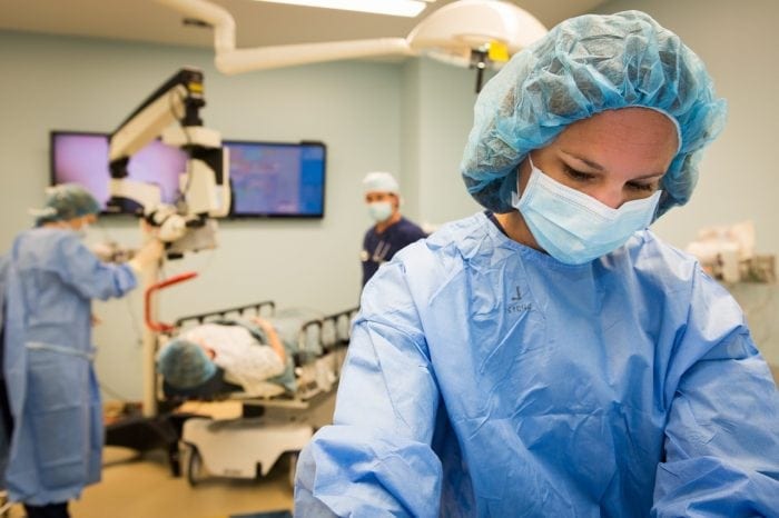 Three doctors in an operating room preparing to perform surgery on a patient who is laying on a hospital bed.