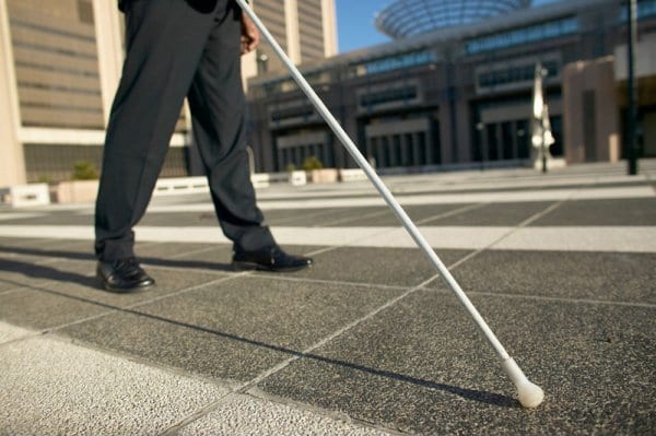 Person from the waist down walking on a sidewalk while using a white cane