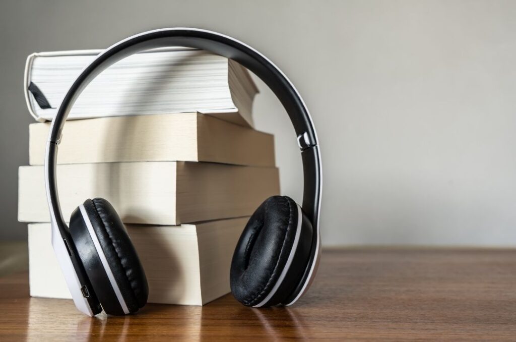A stack of books on a table with a pair of headphones leaning against them.