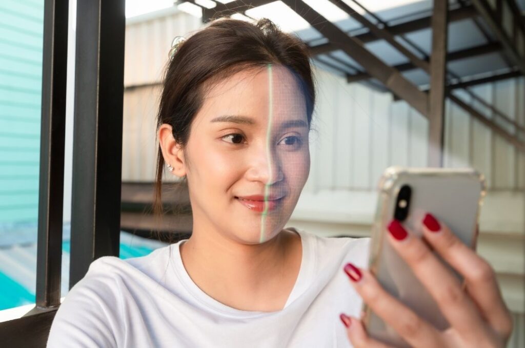 A woman holding up her phone, looking at the screen as it scans half of her face.